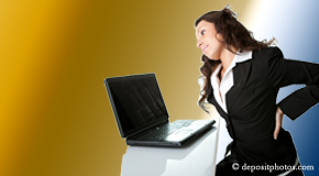 a person Auburn bending over a computer holding her back due to pain